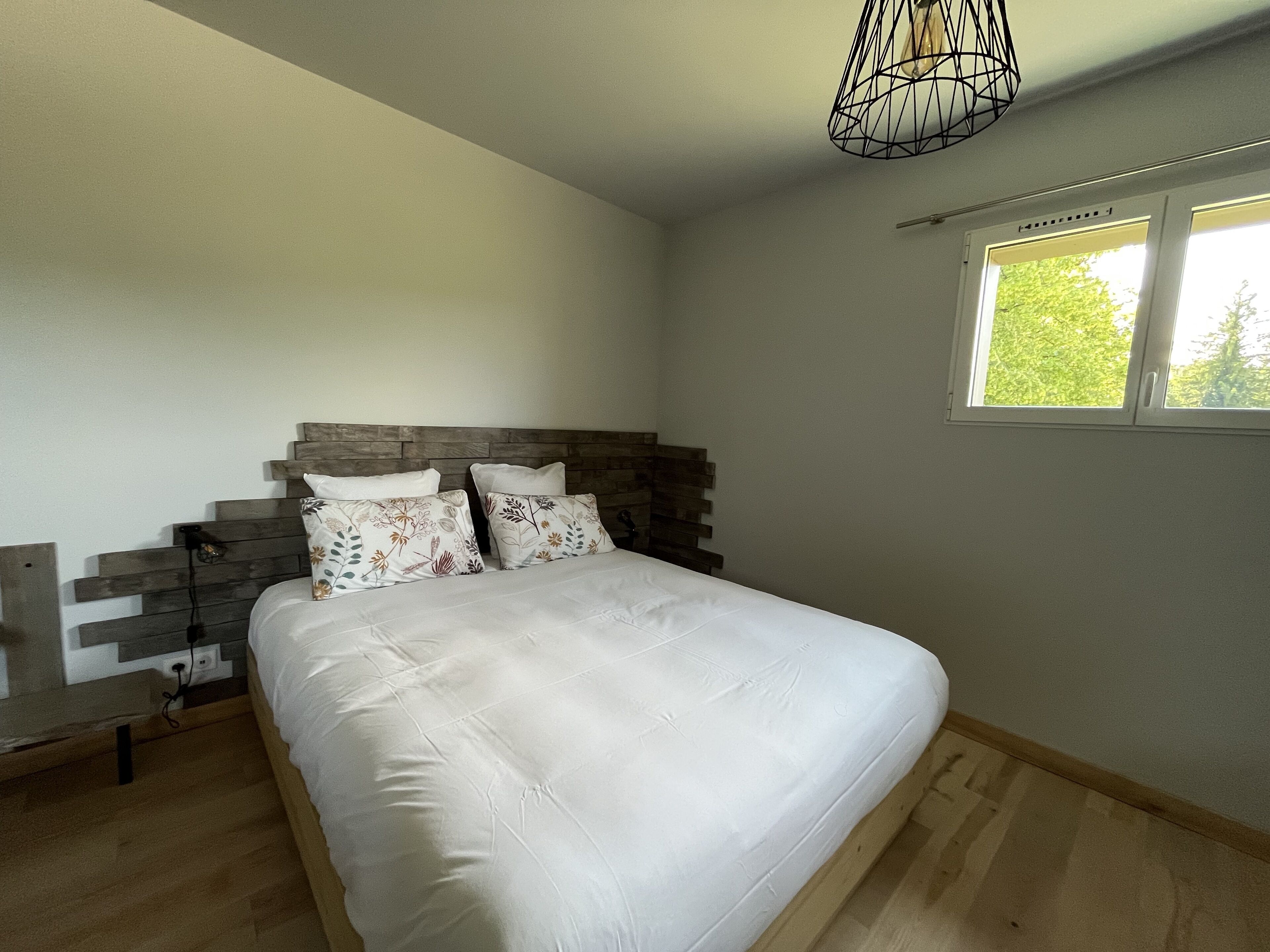 A bedroom with a bed, wooden headboard, and a window with a view of trees.