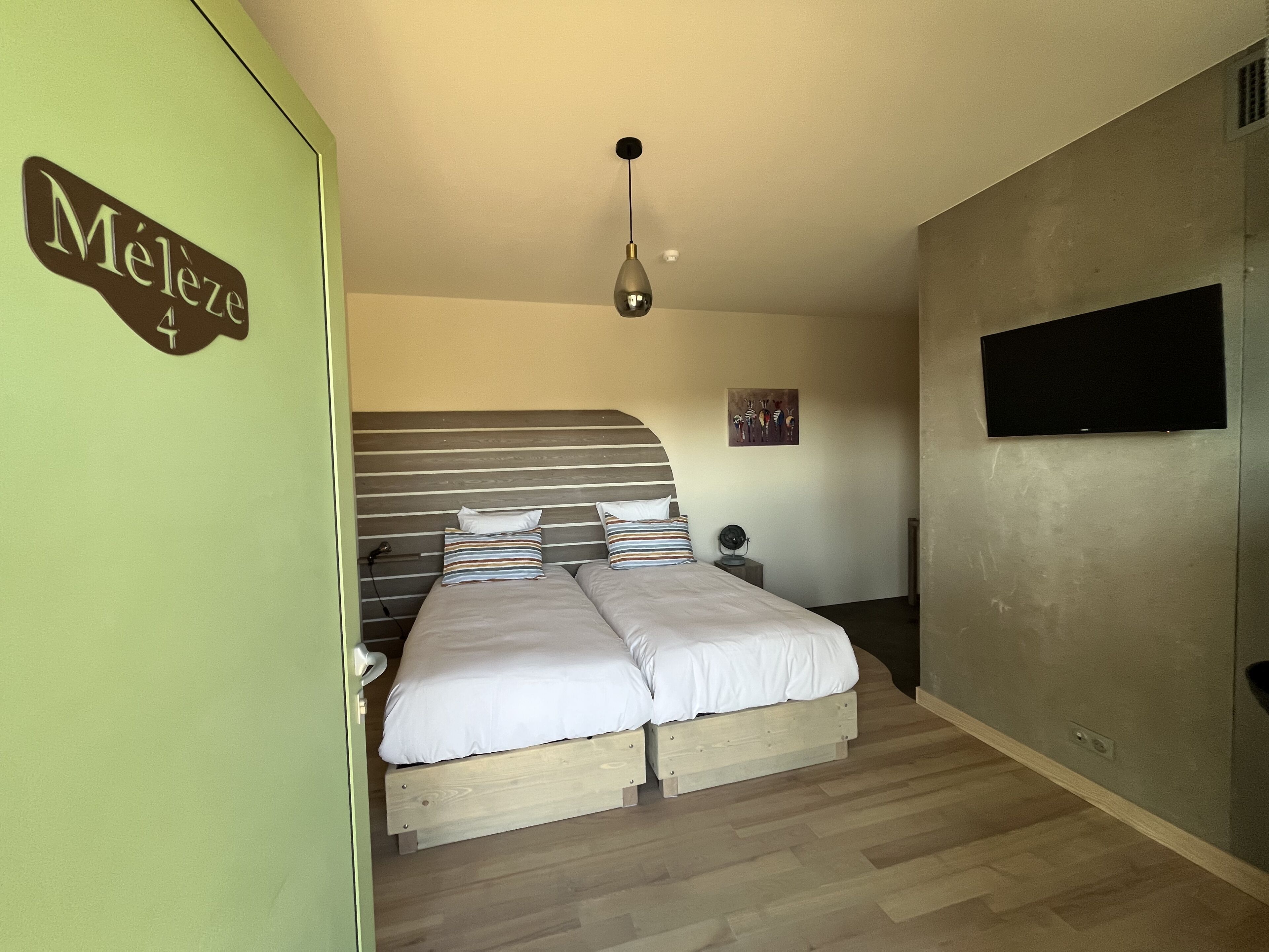 A bedroom with a bed, a bedside table, a lamp, a TV, and a door with a sign.