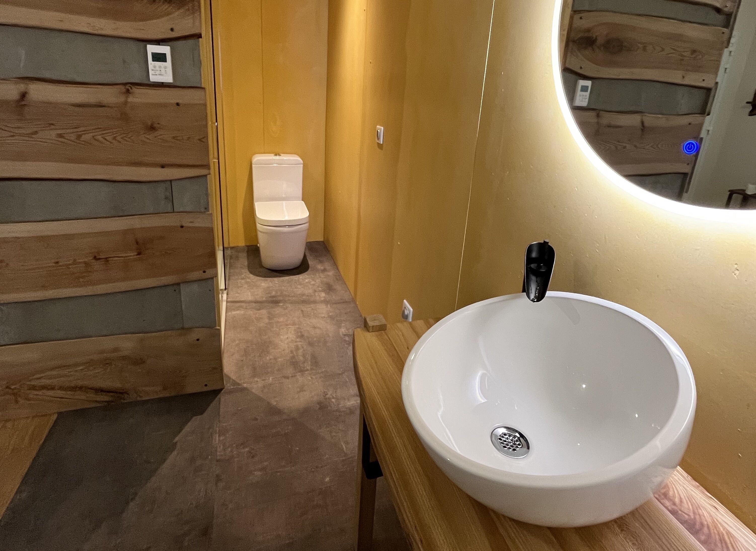 Un baño con pared de madera, un inodoro blanco y un lavabo blanco con grifo negro.