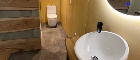 Un baño con pared de madera, un inodoro blanco y un lavabo blanco con grifo negro.