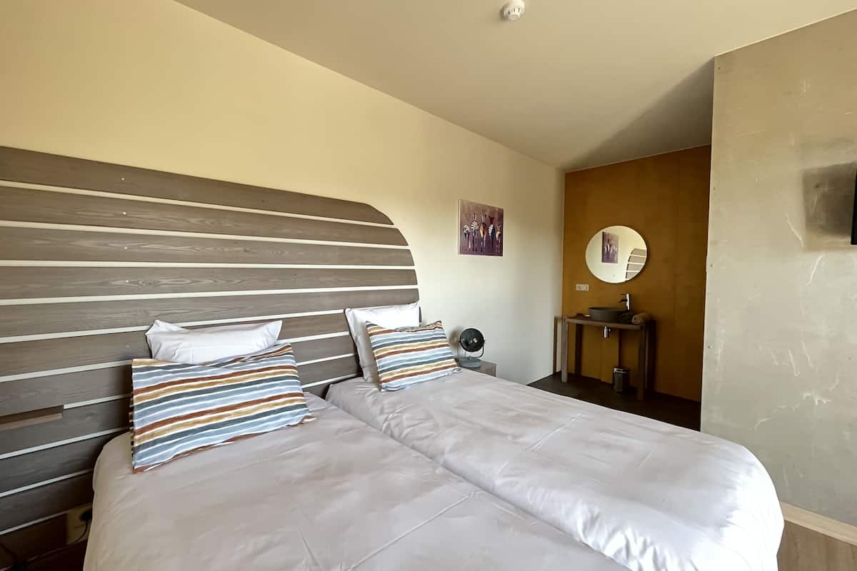 Une chambre d’hôtel comprenant un lit, une table de chevet, un miroir et une œuvre d’art accrochée au mur.