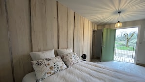 A bedroom with a large bed, wooden panel walls, a ceiling fan, and a view of a balcony. - Hôtel En Tilleul (Pont-du-Navoy)