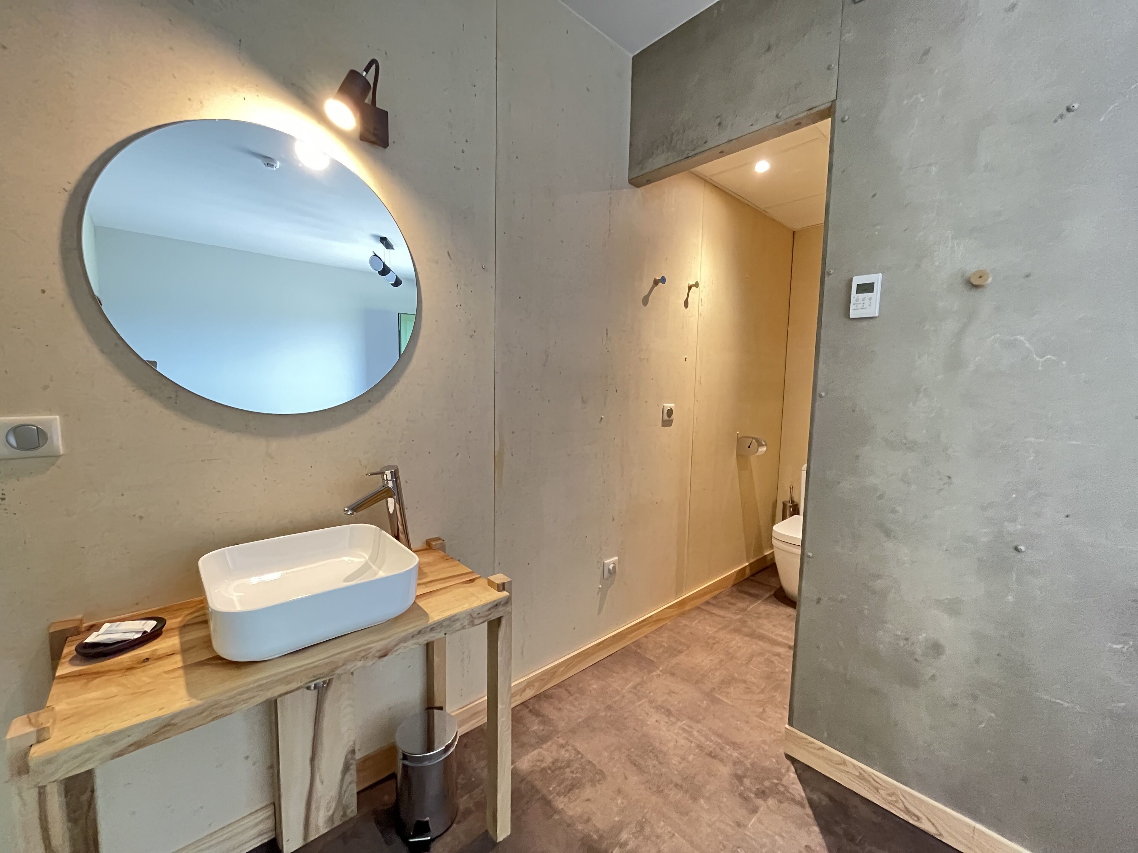 A modern bathroom with a round mirror, a white sink, and a wooden vanity.
