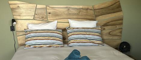 A bed with a wooden headboard, two pillows with striped patterns, a folded blue towel, and a wall socket.