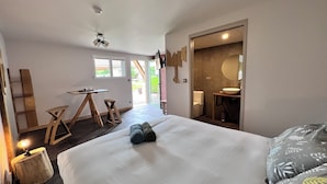 A hotel room with a bed, a desk, a chair, a small table, a mirror, and a bathroom with a sink and toilet. - Hôtel En Tilleul (Pont-du-Navoy)