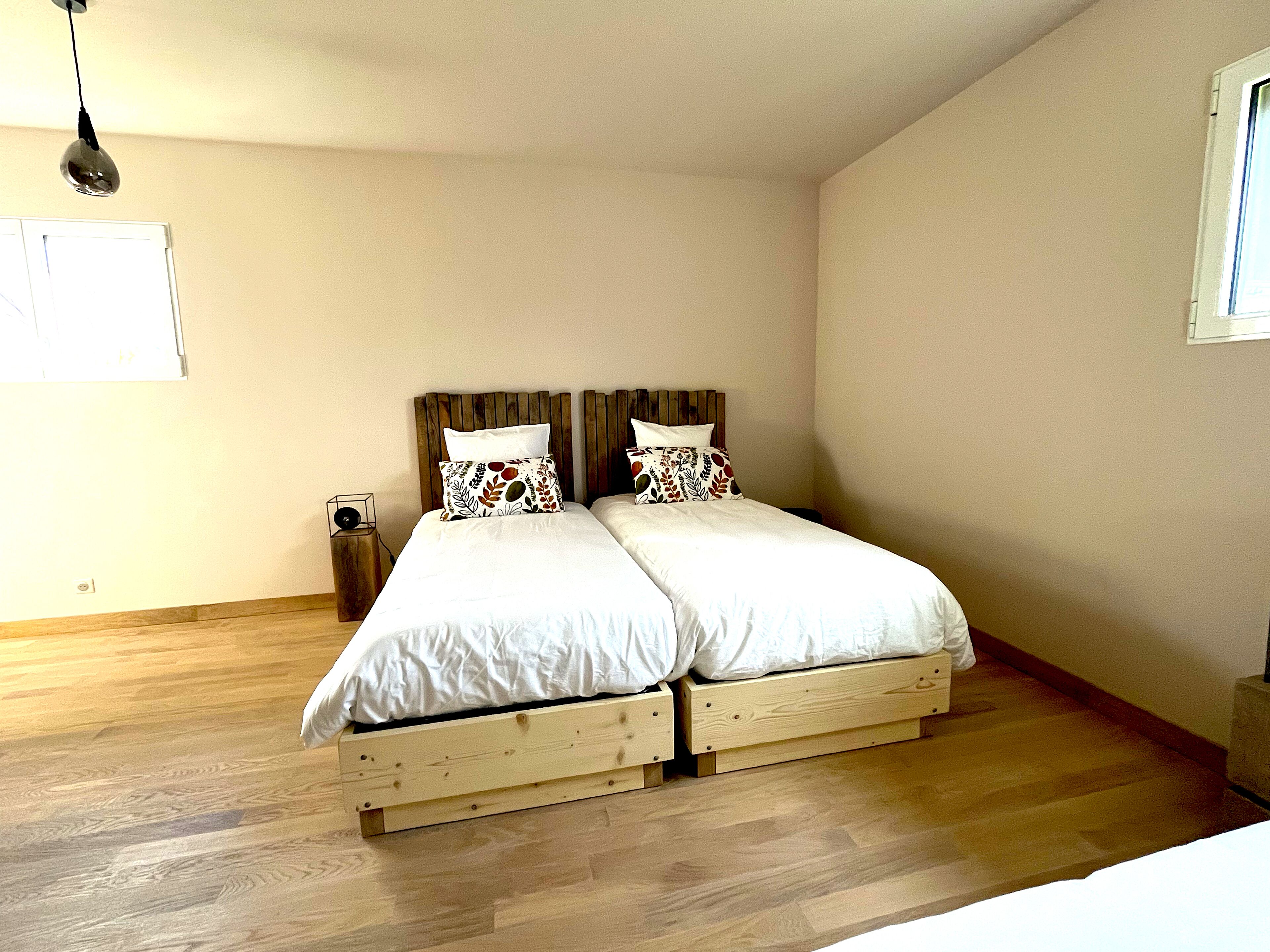 Un dormitorio con una cama de madera, dos almohadas, una mesita de noche y una lámpara colgante.
