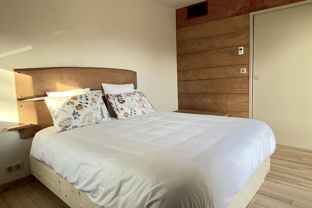 Une chambre à coucher avec une tête de lit en bois, deux coussins à motifs floraux, un couvre-lit blanc et une armoire en bois.