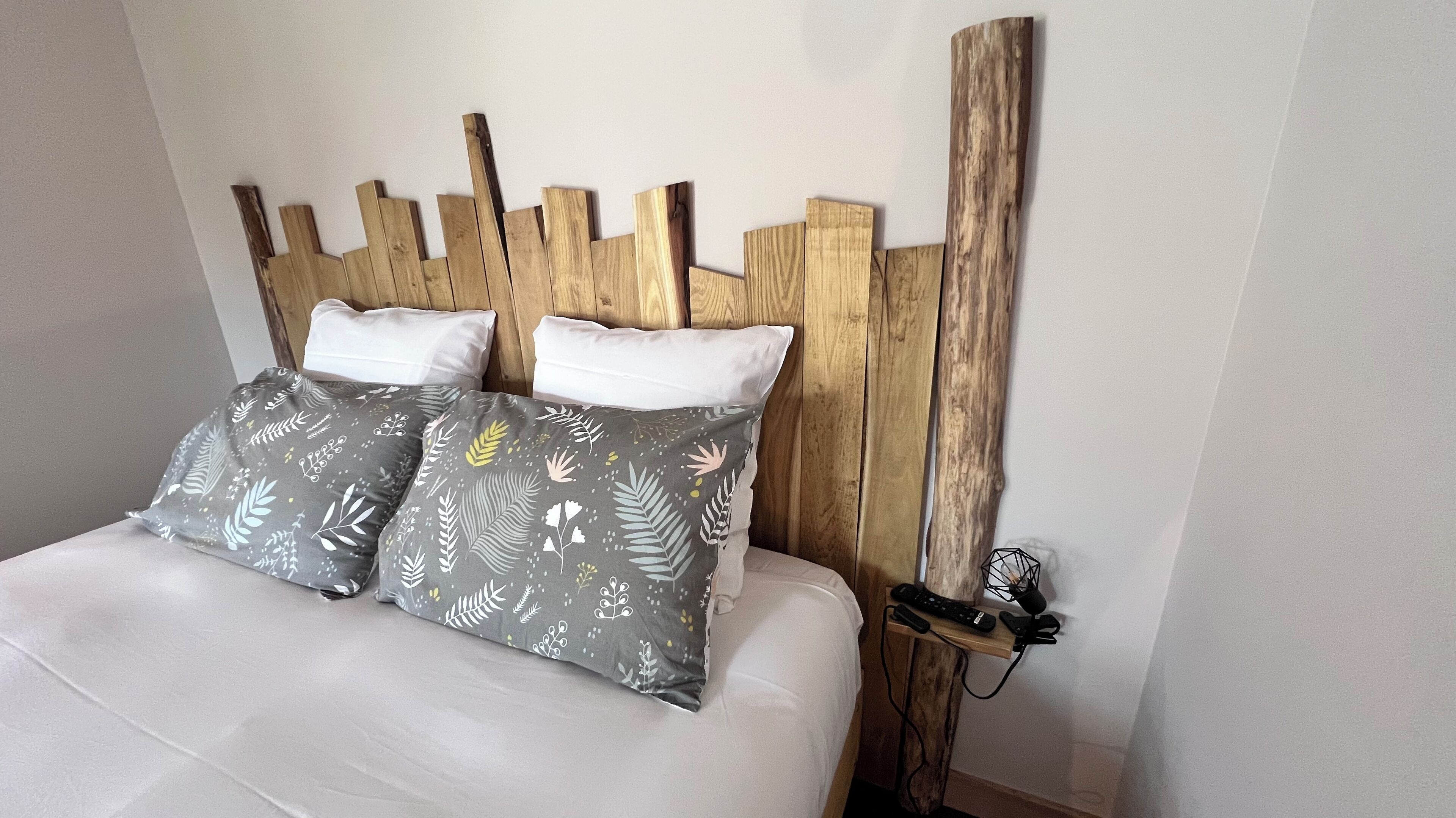 A bed with a wooden headboard, two white pillows, and two gray pillows with a leaf pattern.