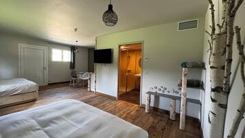 A bedroom with two beds, a TV, a small table, and a shower area.