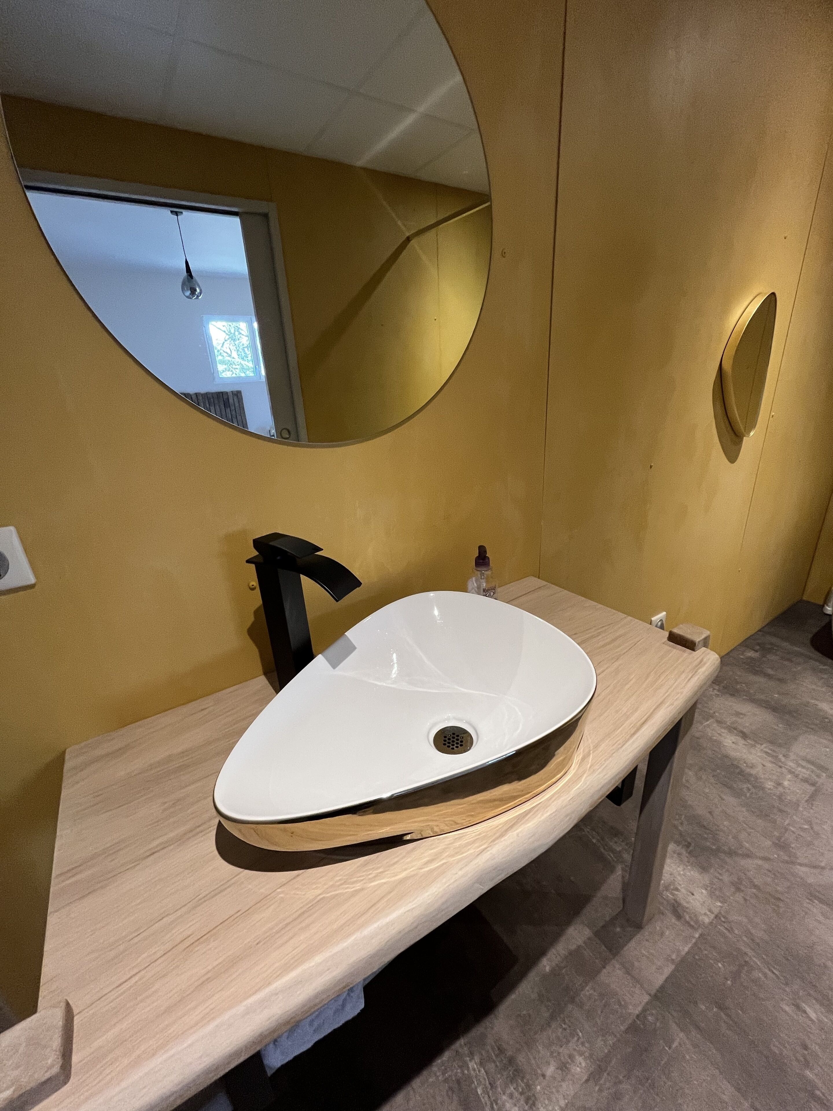 A modern bathroom with a white oval sink, a black faucet, and a round mirror.