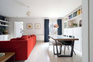 A modern living room with a red sofa, a dining table with chairs, and a kitchen area visible through a glass door.