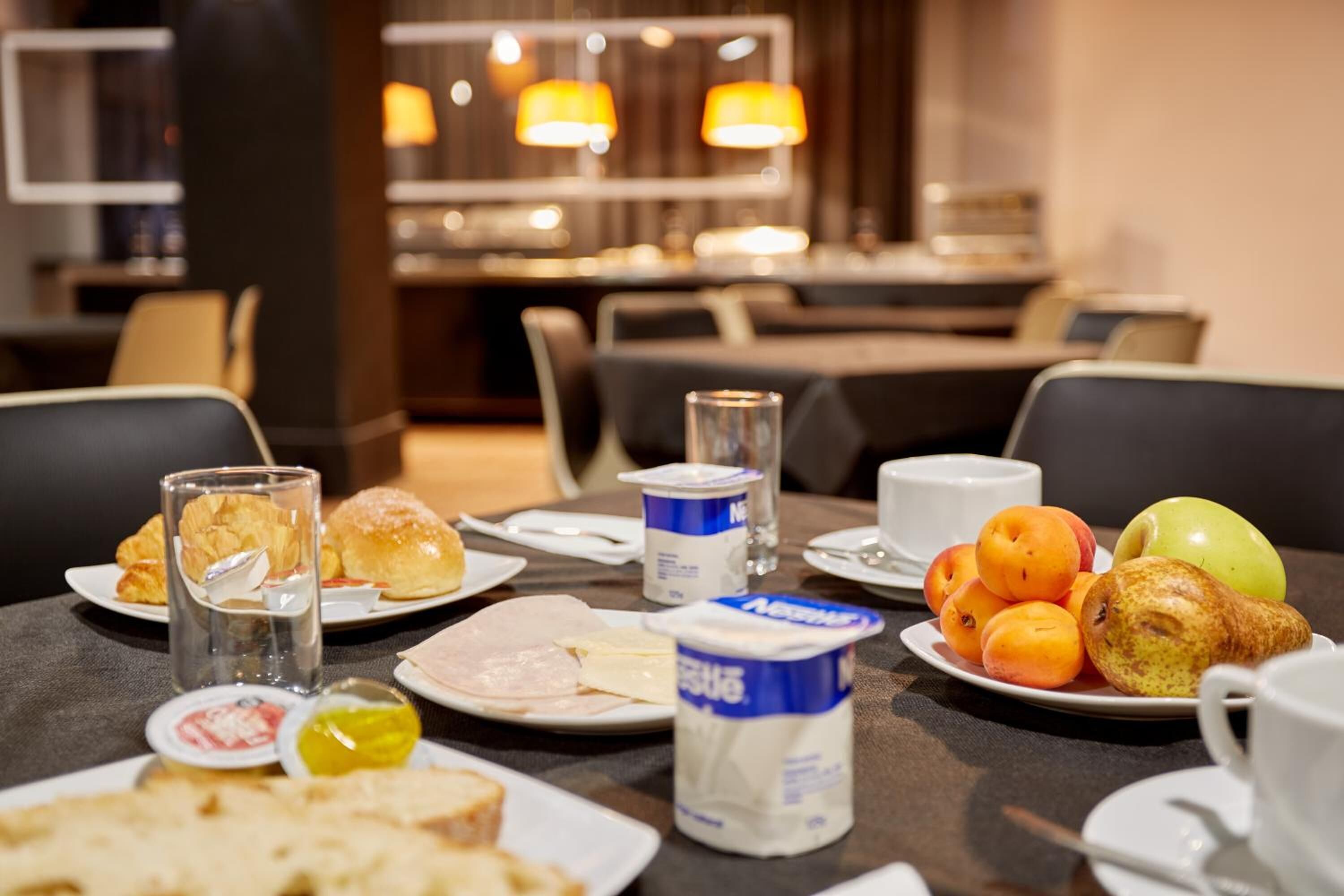 Une table de petit-déjeuner avec des assiettes remplies de nourriture, notamment des viennoiseries, des fruits et des produits laitiers, dans la salle à manger d’un hôtel.