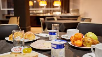 Une table de petit-déjeuner avec des assiettes remplies de nourriture, notamment des viennoiseries, des fruits et des produits laitiers, dans la salle à manger d’un hôtel.