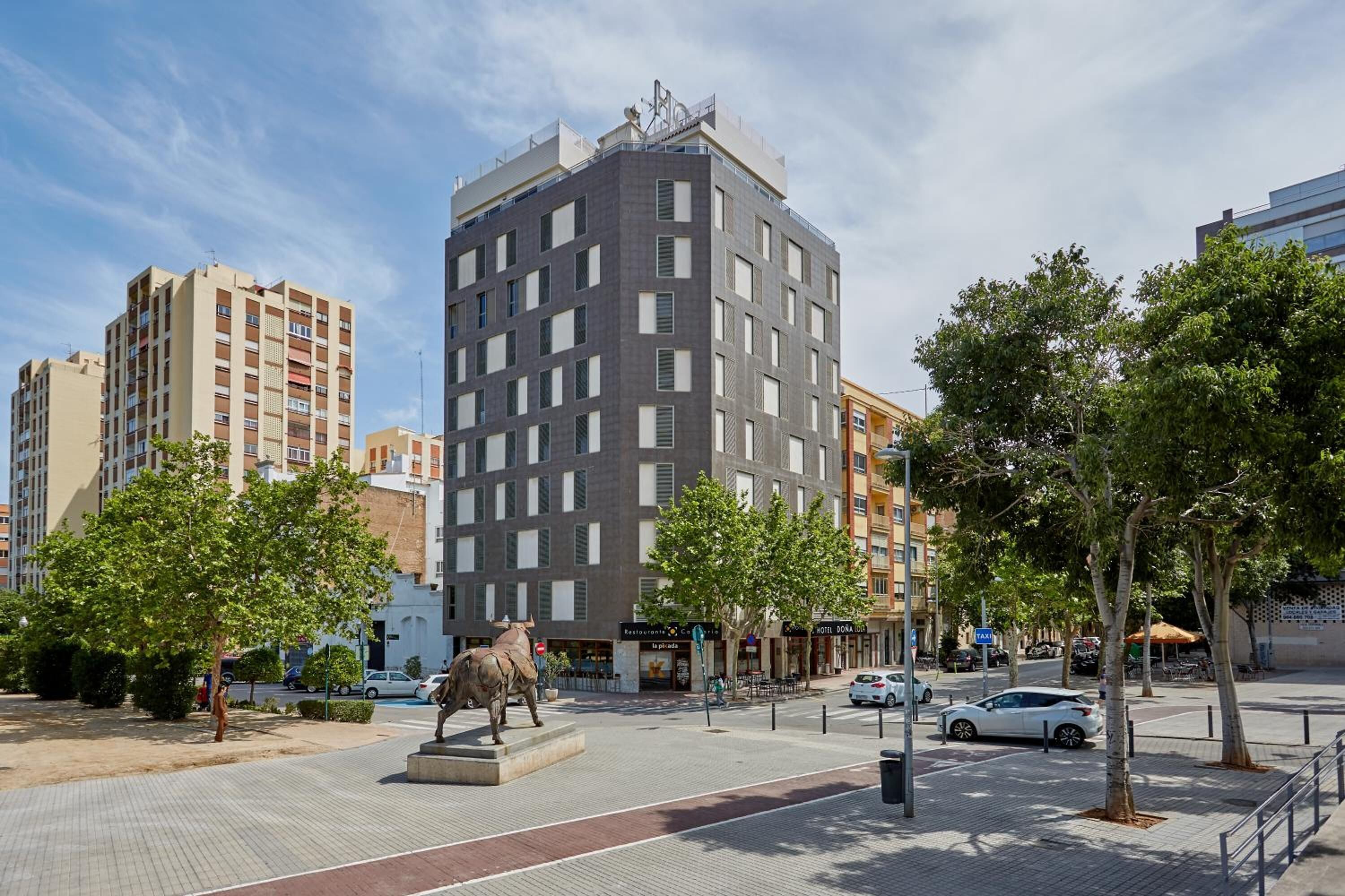 Un bâtiment moderne doté d’une cour intérieure, entouré d’arbres et orné d’une statue.