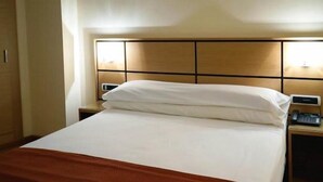Una habitación de hotel con una cama, una mesita de noche y una lámpara.