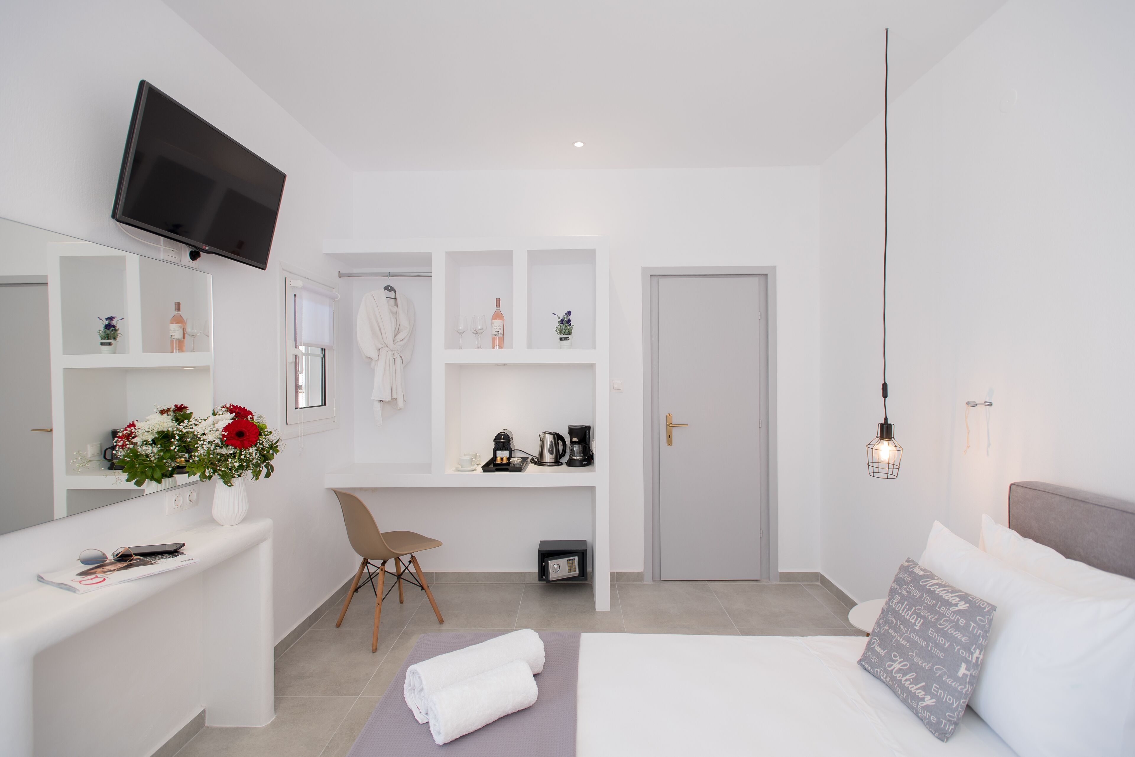 Una habitación de hotel moderna con televisión de pantalla plana, un escritorio con silla, cama con ropa blanca y un estante con adornos.