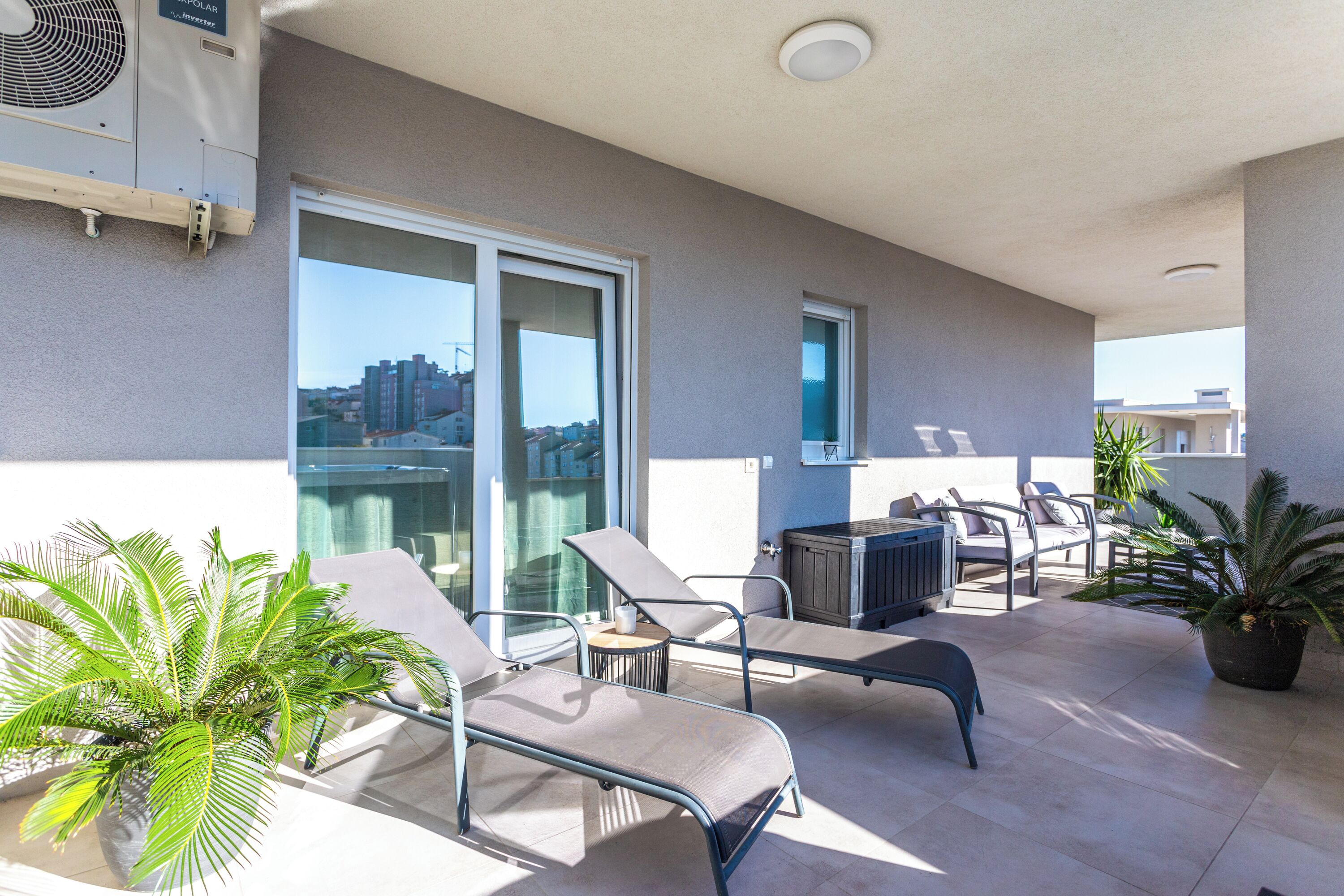 A balcony with lounge chairs, a table, and potted plants.