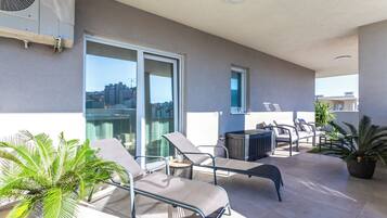 A balcony with lounge chairs, a table, and potted plants.