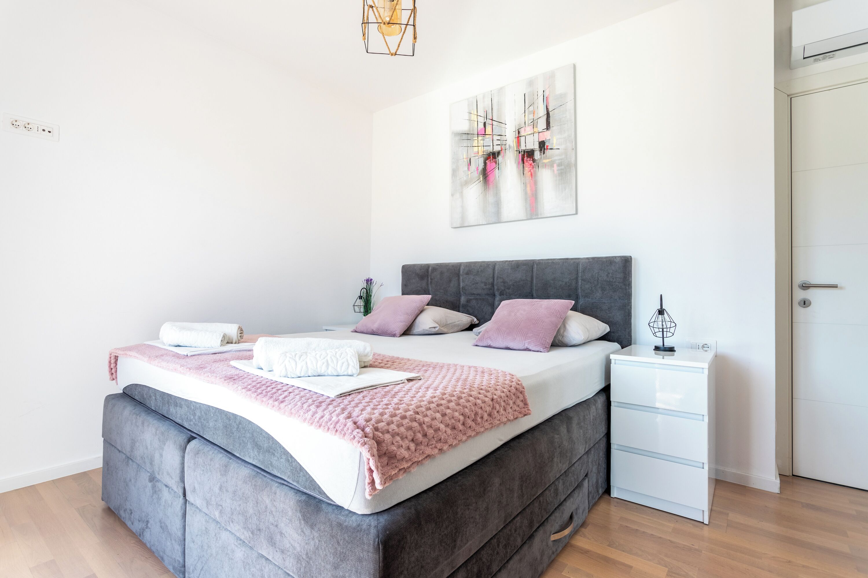 A modern bedroom with a grey upholstered bed, a white bedside table, and a grey headboard.