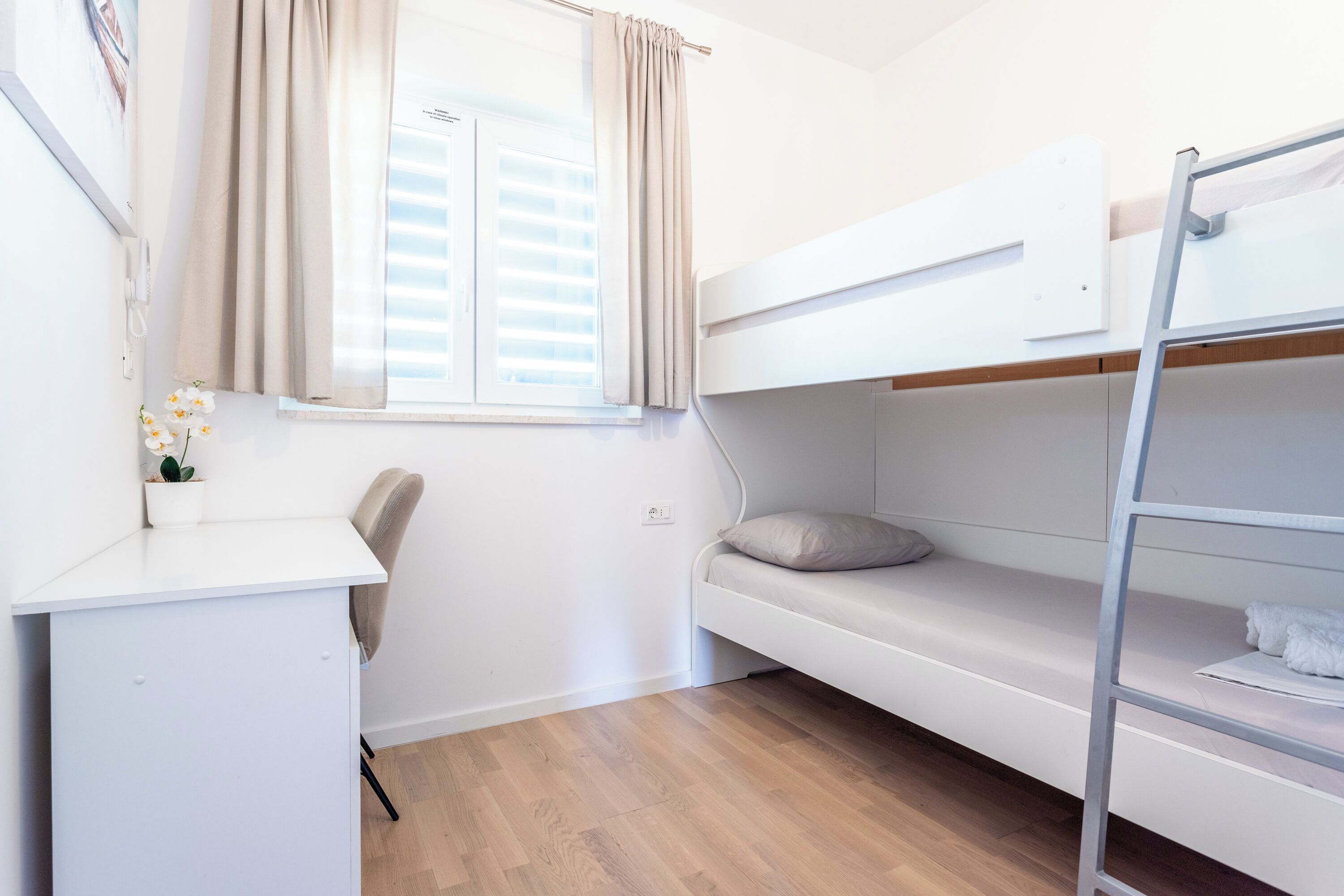 Habitación con literas, un escritorio, una silla, una ventana con cortinas y una pequeña planta.
