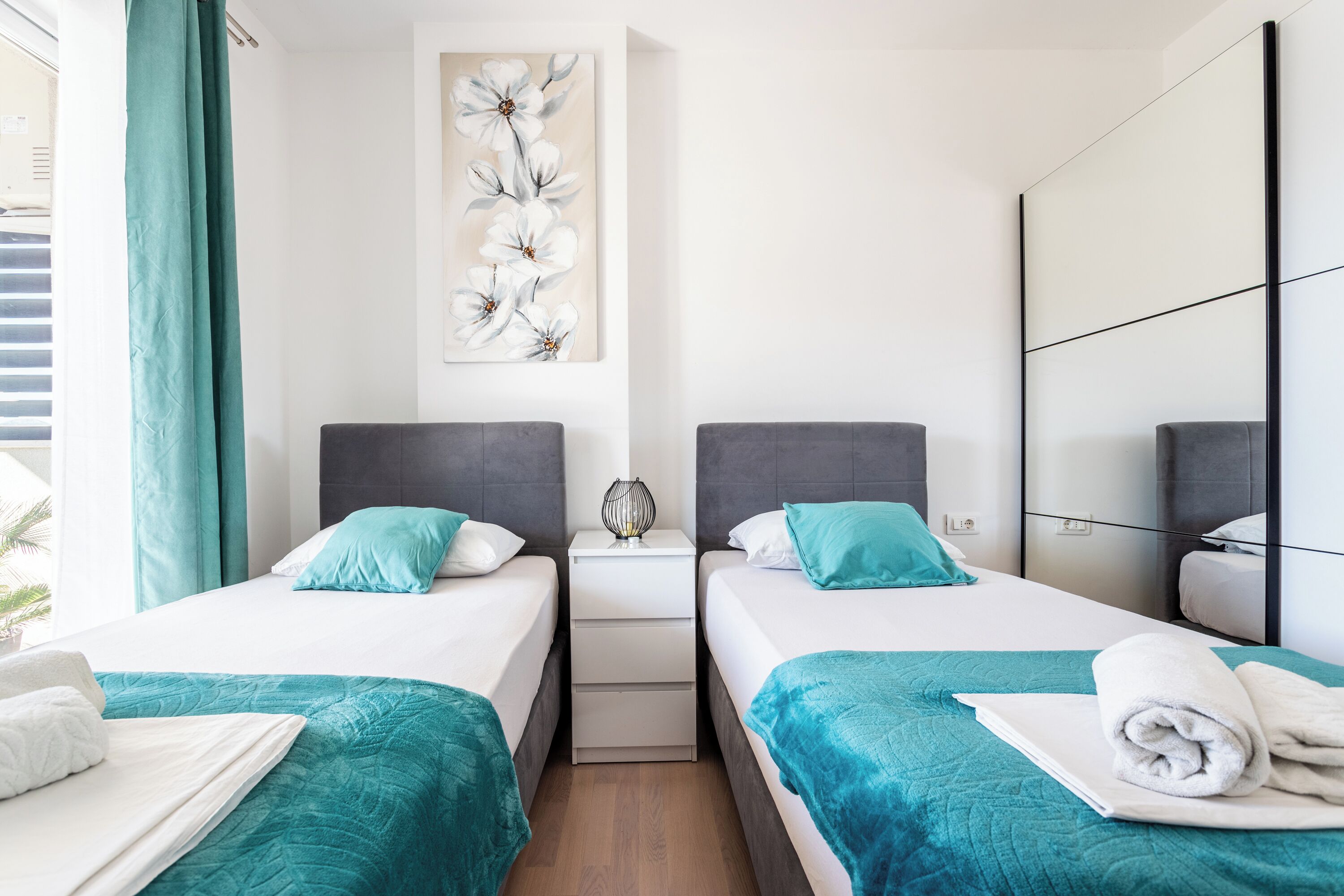 A hotel room with two beds, teal bedding, a large floral artwork on the wall, and a modern design.