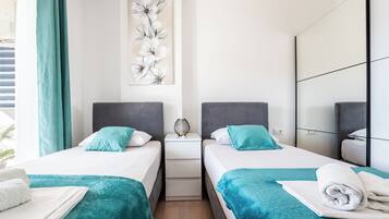 A hotel room with two beds, teal bedding, a large floral artwork on the wall, and a modern design.