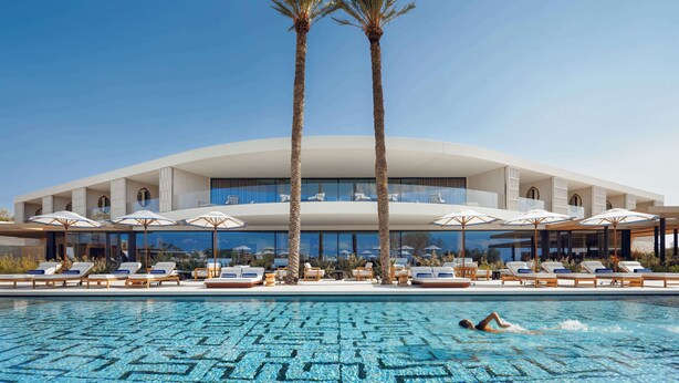 A modern hotel with a pool, palm trees, and sun loungers.