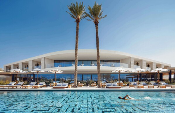 A modern hotel with a pool, palm trees, and sun loungers.