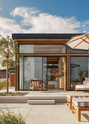 A modern house with a patio area featuring a wooden table and chairs, a sofa, and a large umbrella.