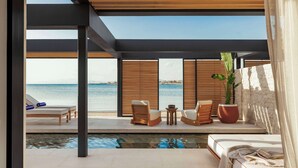 A modern outdoor lounge area with a pool, wooden furniture, and a view of the sea.