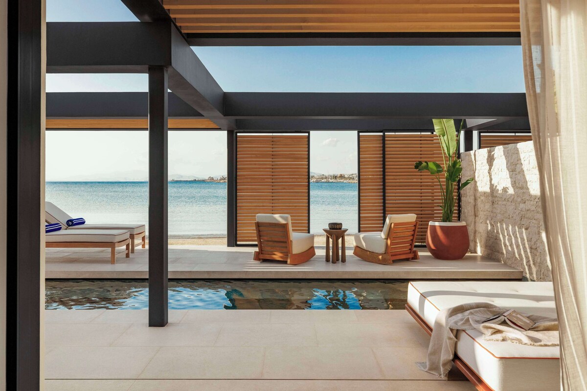 Ett modernt utomhusområde med loungekänsla, en pool, trämöbler och utsikt över havet.