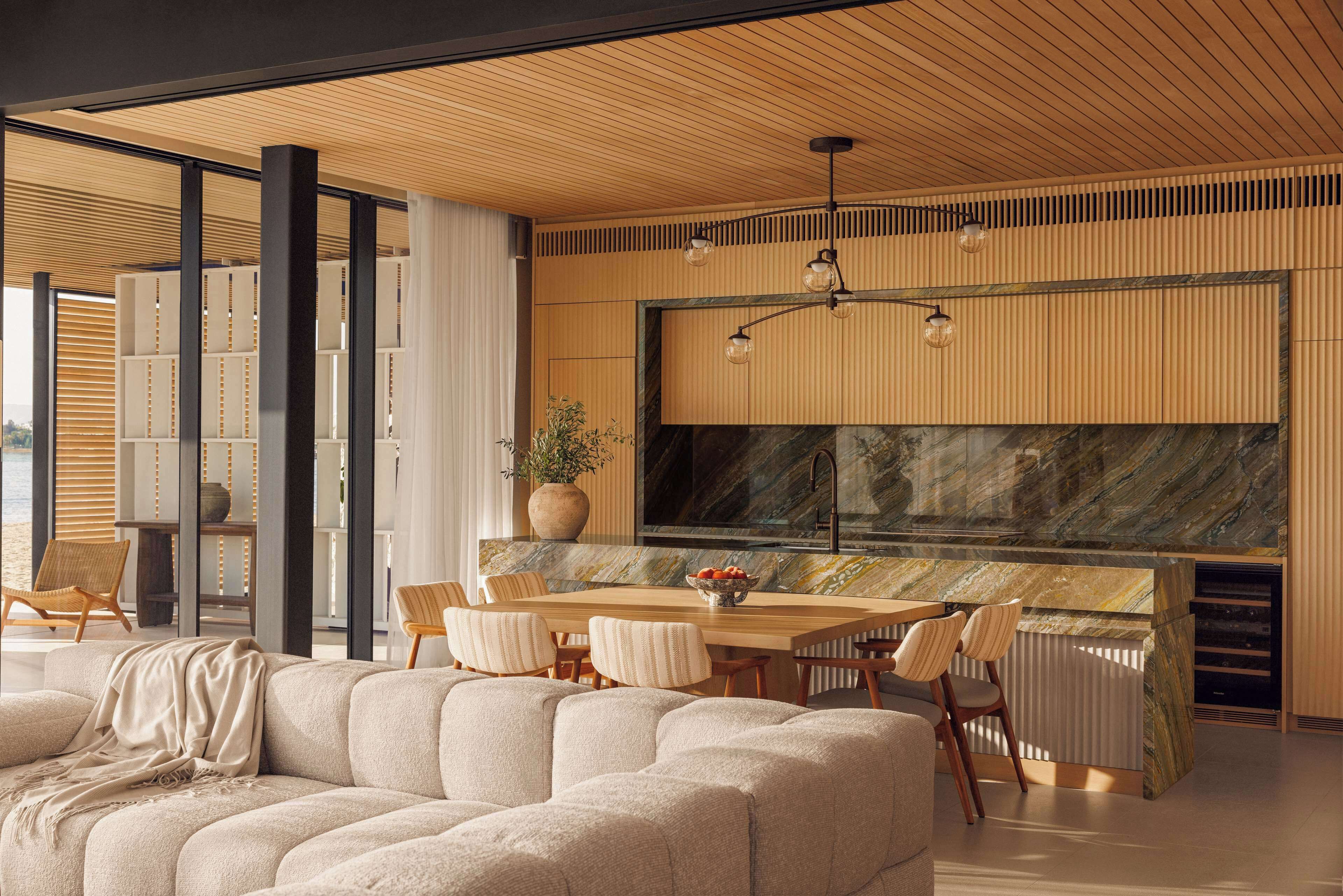 Una cocina moderna con una isla grande, techo de madera y un amplio ventanal con vistas a un paisaje urbano.