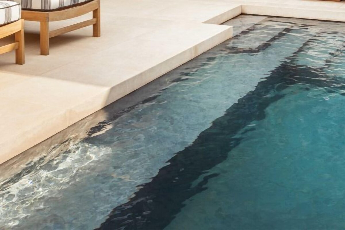 A pool with clear water, a wooden chair, and a stone ledge.