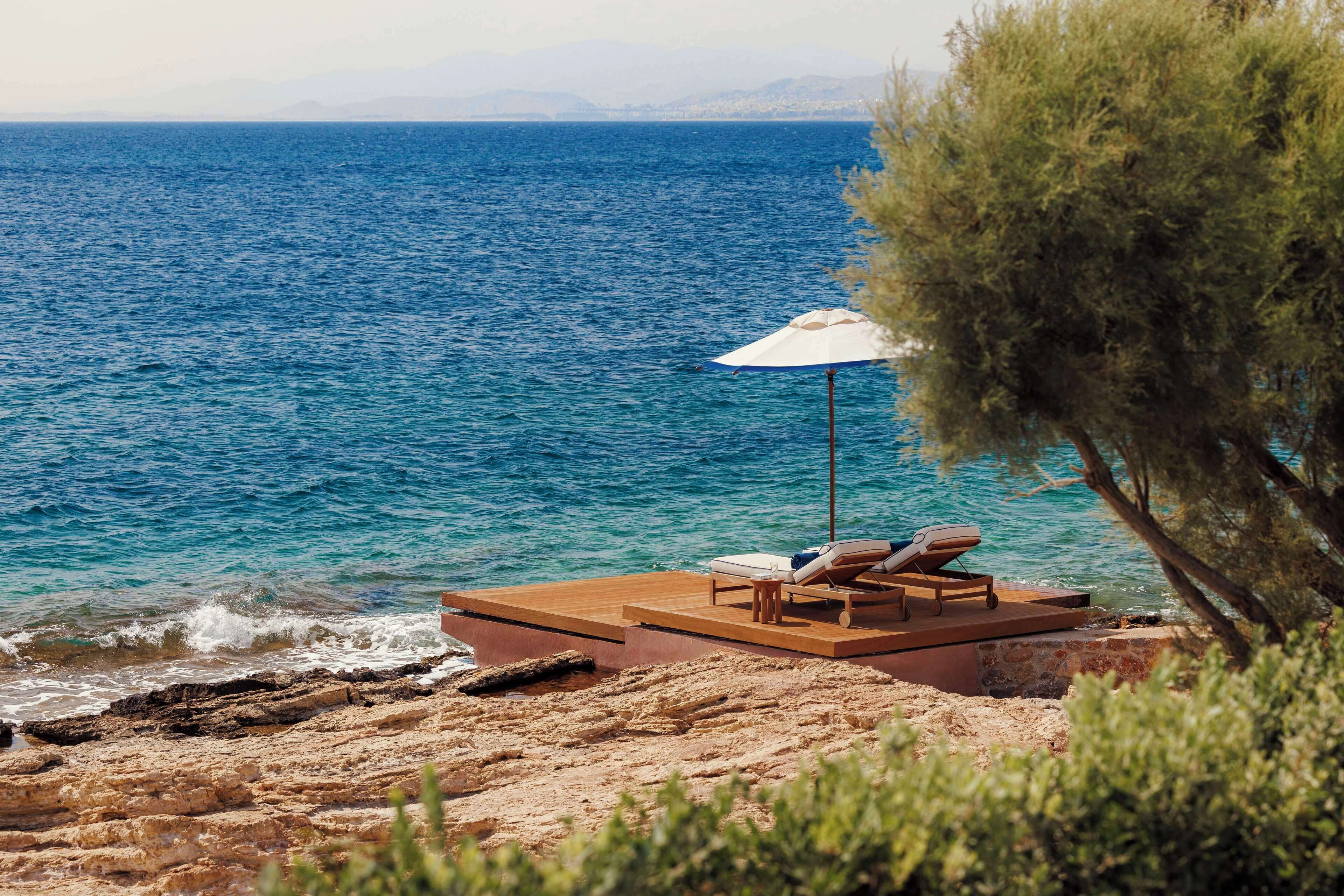 A wooden deck with two lounge chairs and a white umbrella overlooking a body of water.