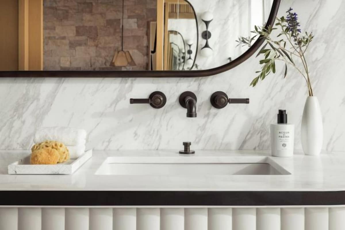A bathroom with a white marble sink, a black faucet, and a mirror with a curved frame.