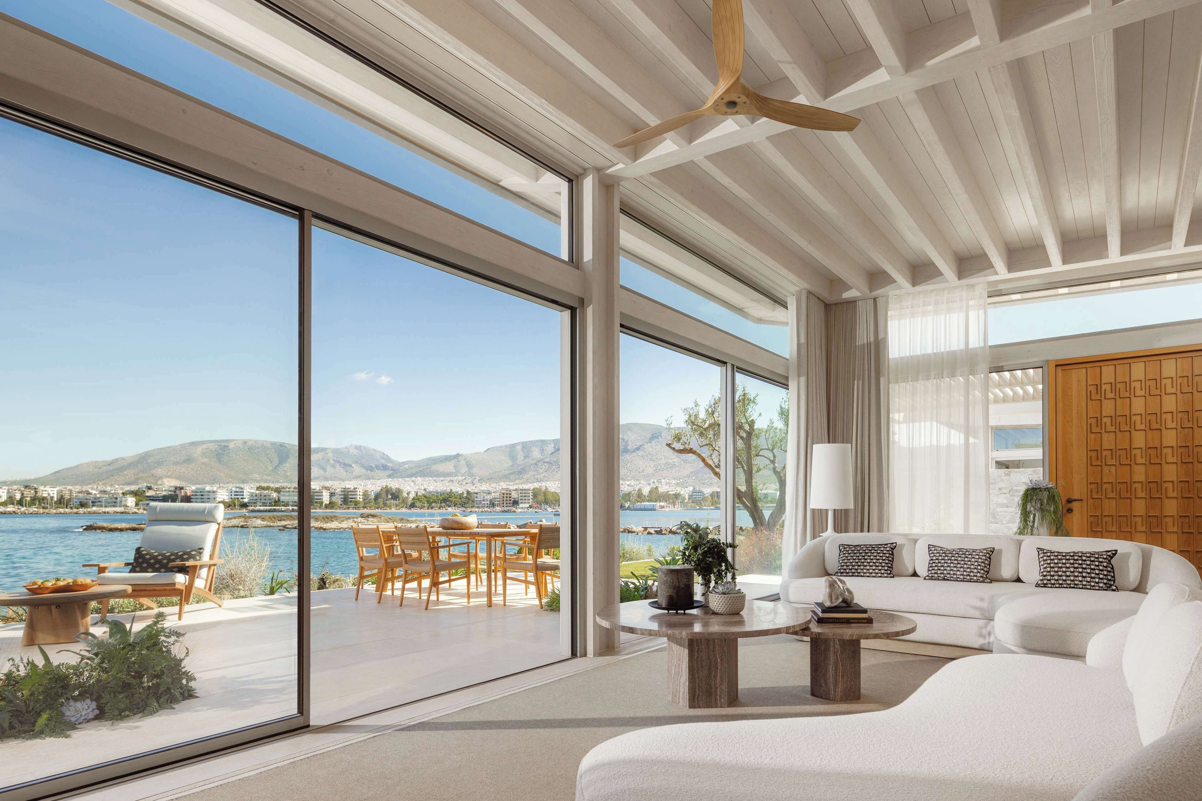 Un salón moderno con un gran ventanal que da a un balcón con vistas al agua y montañas.