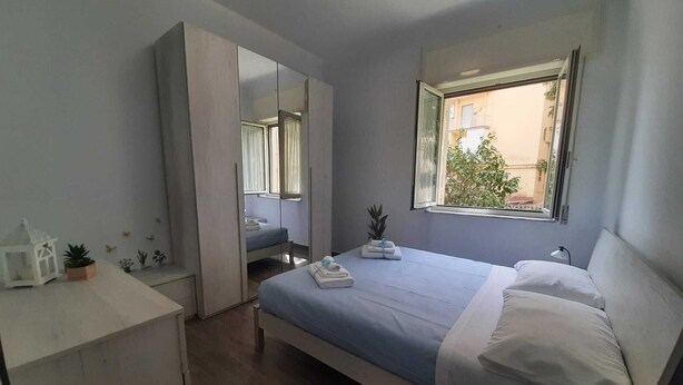 A bedroom with a bed, a mirror, a window, and a small desk.