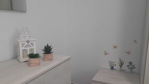 A minimalist room with a white dresser, a small table with two potted plants, a white lantern, and butterfly wall decals.