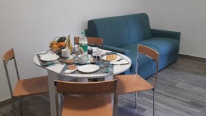 A dining area with a round table set for four, surrounded by chairs. A blue sofa is against the wall, and there are small framed pictures above it.