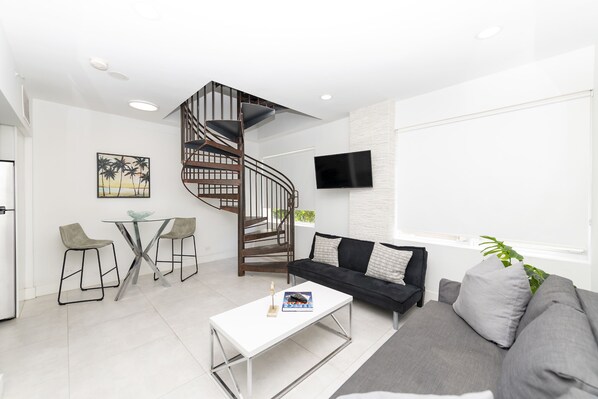 Una sala de estar moderna con una escalera en espiral, un televisor de pantalla plana, un sofá y una mesa de centro.