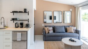 A modern kitchen with a sink, kettle, and toaster, a grey sofa with cushions, and a round coffee table.