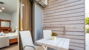 A modern room with a bed, a small table with a potted plant, and a sliding glass door leading to an outdoor area with a wooden deck. - Yianna Studios (Rhodes)