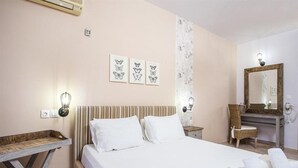 A hotel room with a bed, a nightstand, a mirror, and a wall-mounted light fixture. - Yianna Studios (Rhodes)