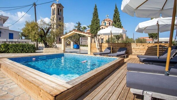 A swimming pool with lounge chairs and umbrellas, a church, and a sign for 'YIANNAS STUDIOS'. - Yianna Studios (Rhodes)