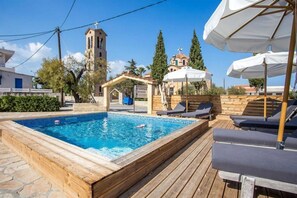 Una piscina con sillas de descanso y sombrillas, una iglesia y un cartel que dice 'YIANNAS STUDIOS'.