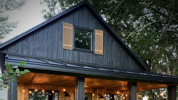 Une maison en bois avec un porche, une porte verte et le numéro « 2090B » peint sur le mur.
