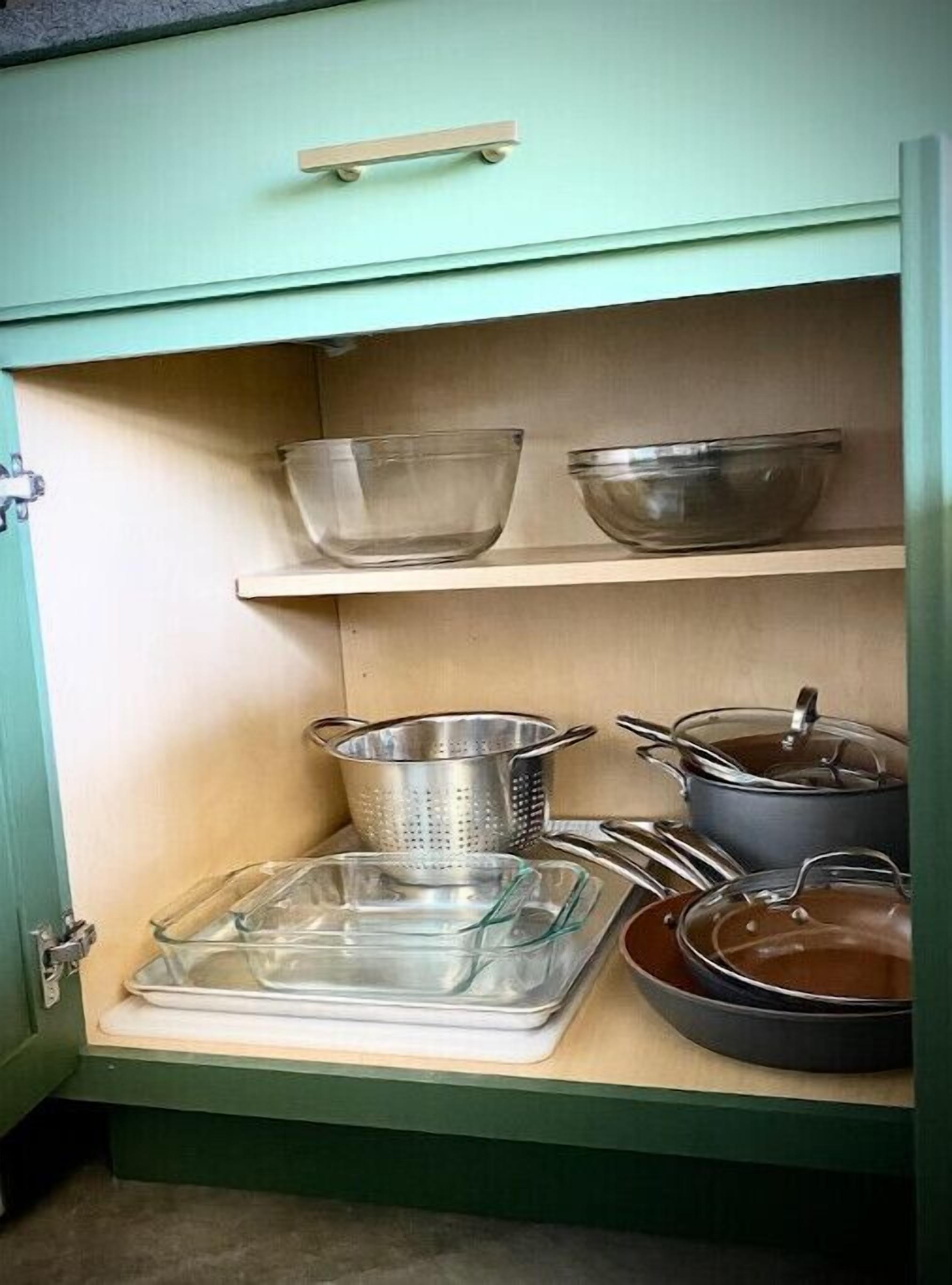 A kitchen with a green cabinet, a metal colander, a glass baking dish, and a pot.
