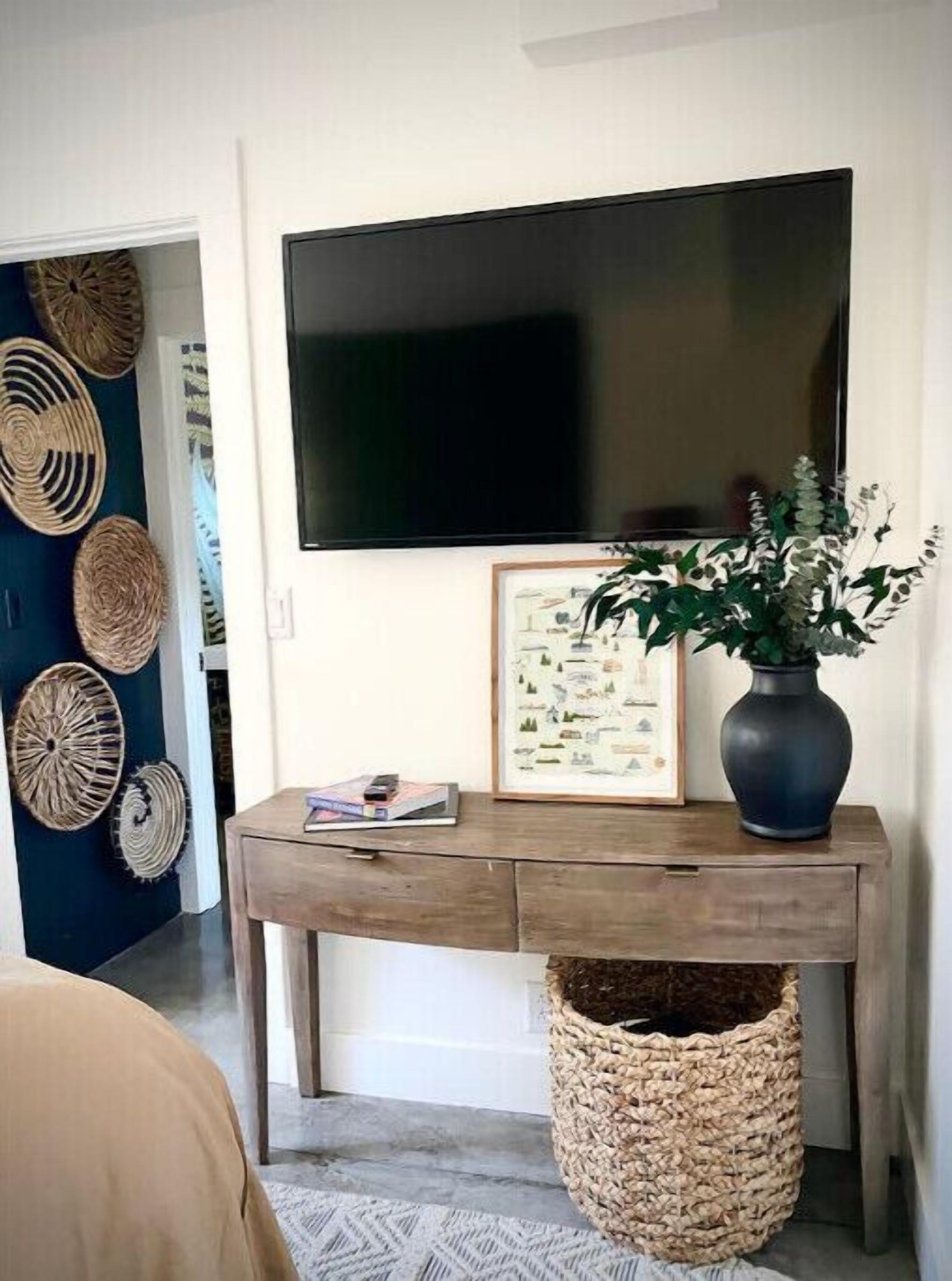A room with a wooden desk, a framed picture, a vase with plants, and a woven basket.