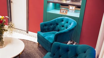 A room with teal armchairs, a white table, and a green shelf with decorative items.