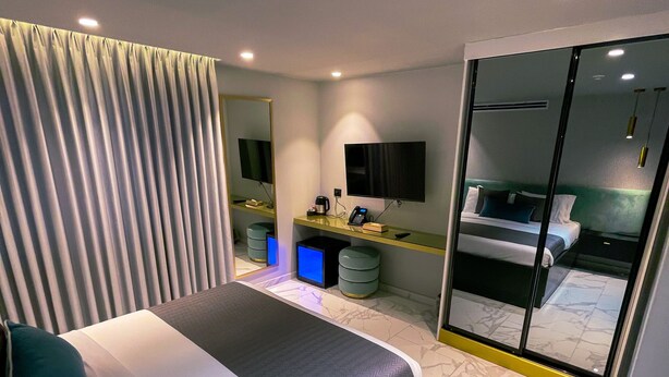 Une chambre d’hôtel moderne dotée d’un grand lit, d’un bureau avec un ordinateur, d’un miroir et d’une porte-fenêtre coulissante donnant sur un balcon.